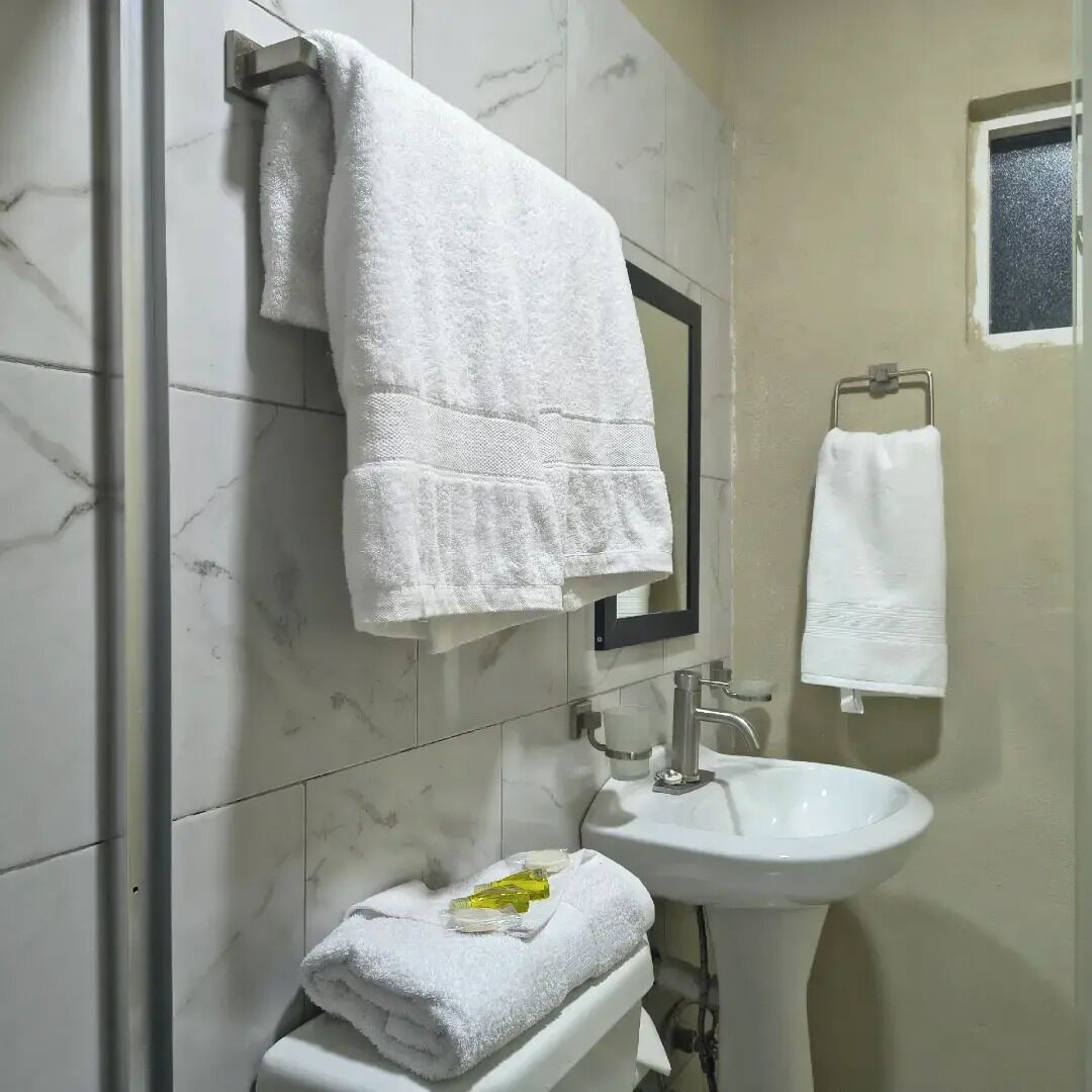 A bathroom with a marble wall, a sink, and two towels hanging on the wall.