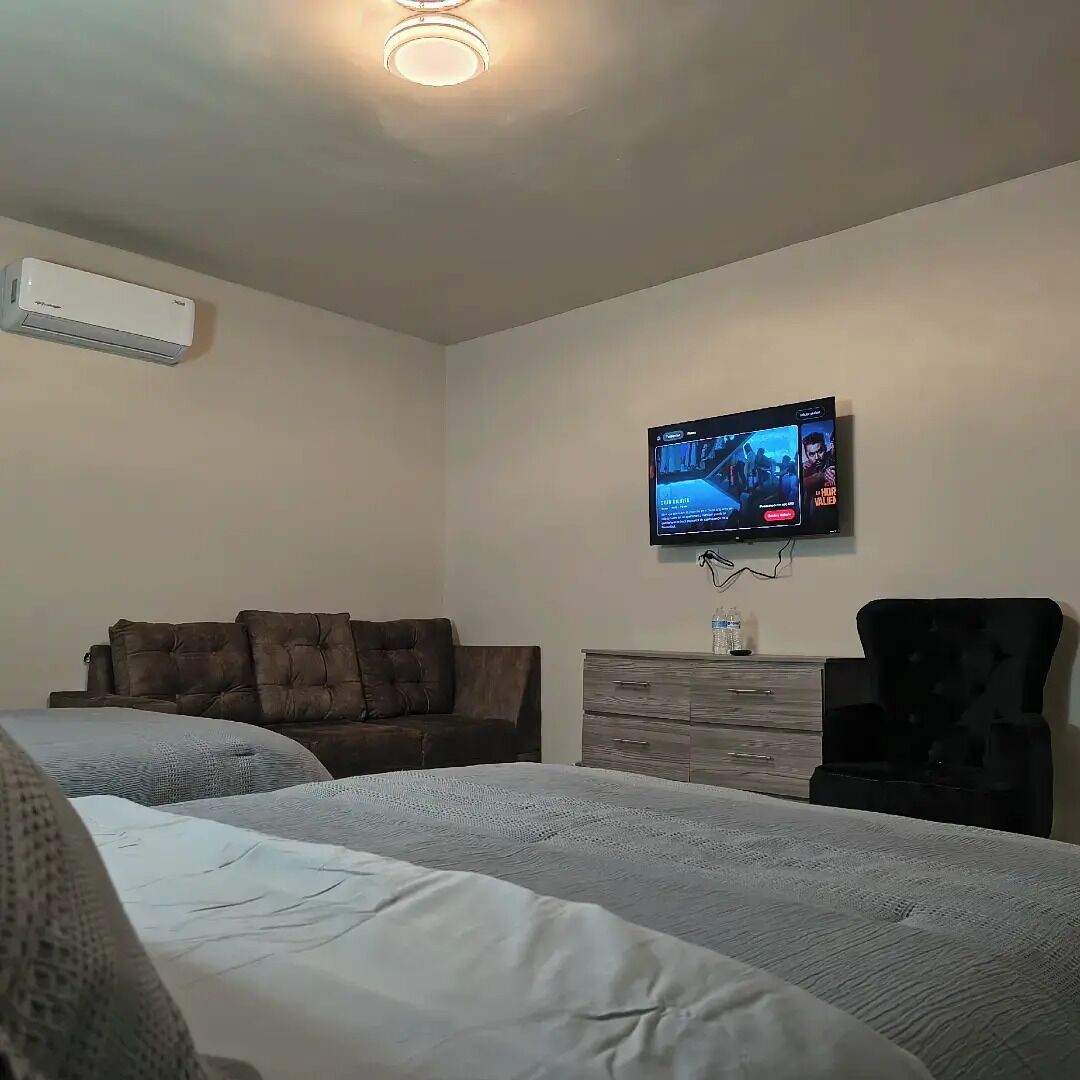 Un dormitorio con dos camas, un televisor en la pared, un aparador y un aire acondicionado.