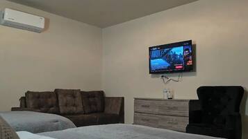 Un dormitorio con dos camas, un televisor en la pared, un aparador y un aire acondicionado.