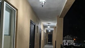 Un pasillo con suelo de baldosas, puertas negras y barandilla de balcón.