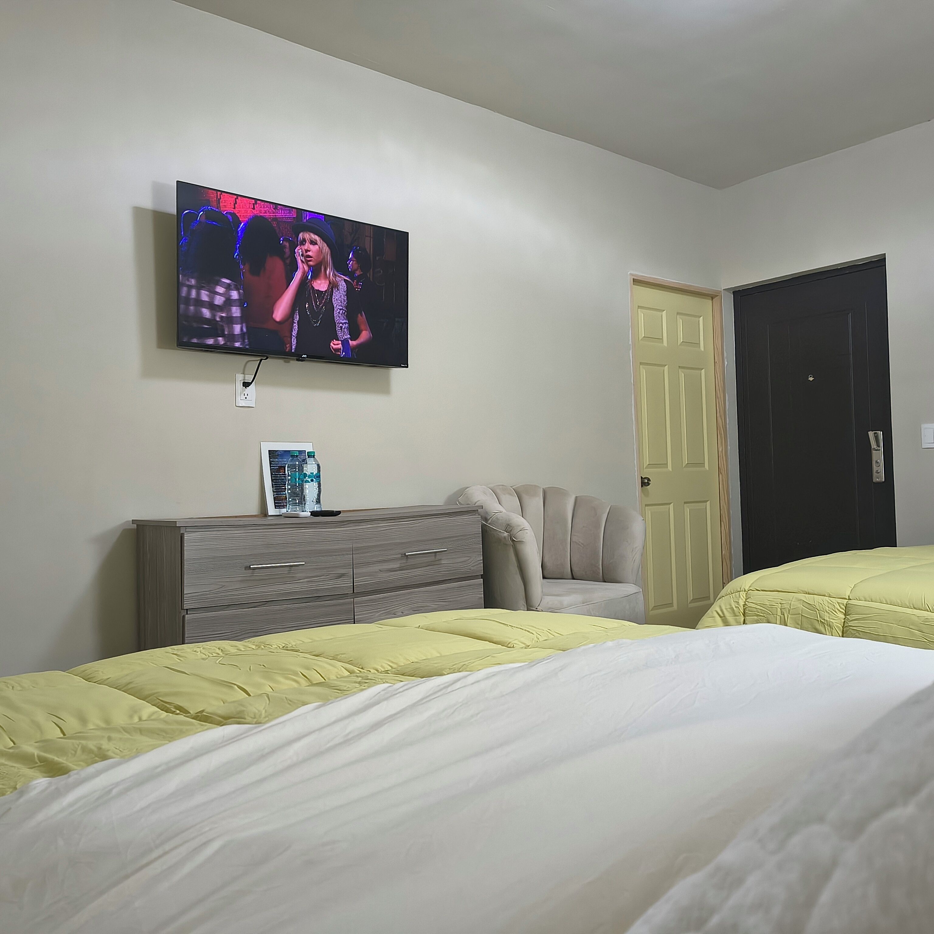 A bedroom with two beds, a TV on the wall, a dresser, and a door.