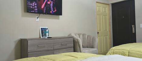 A bedroom with two beds, a TV on the wall, a dresser, and a door.
