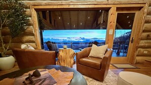 Ein gemütliches Blockhaus-Interieur mit einer Ledersofa, einem runden Tisch und Bergblick durch ein großes Fenster.