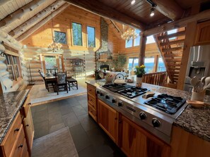 A log cabin interior with a kitchen, dining area, and a view of the outdoors.