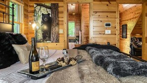 Ein Holzblockhaus-Interieur mit einem Bett, einer Weinflasche und einer Platte mit Snacks.