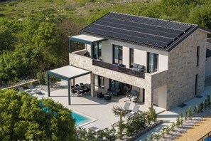 Une maison moderne à deux étages, dotée d’un ensemble de panneaux solaires sur le toit, d’un espace extérieur aménagé et couvert, et d’une piscine.