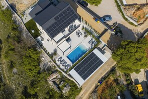 Vue aérienne d’un bâtiment moderne doté d’une piscine, de panneaux solaires et d’un espace de détente extérieur.