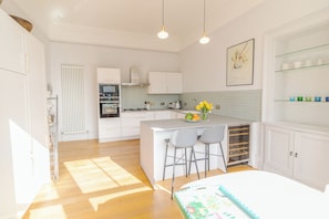 A modern kitchen with white cabinetry, a central island with bar stools, a built-in oven, and a radiator. - LUXURY HERITAGE TOWNHOUSE ︱KING BED ︱NEAR BOTANICS (Edinburgh)