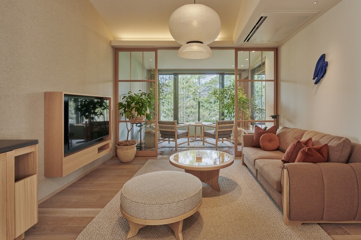 Uma sala de estar moderna com televisão, sofá, mesa de centro e uma janela grande.