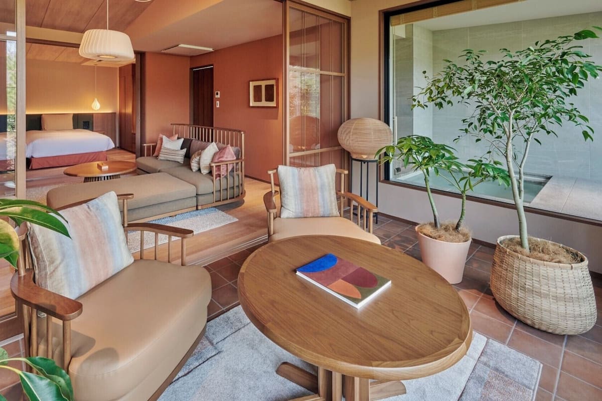 Quarto de hotel moderno com cama, sofá, mesa de jantar e plantas em vasos.
