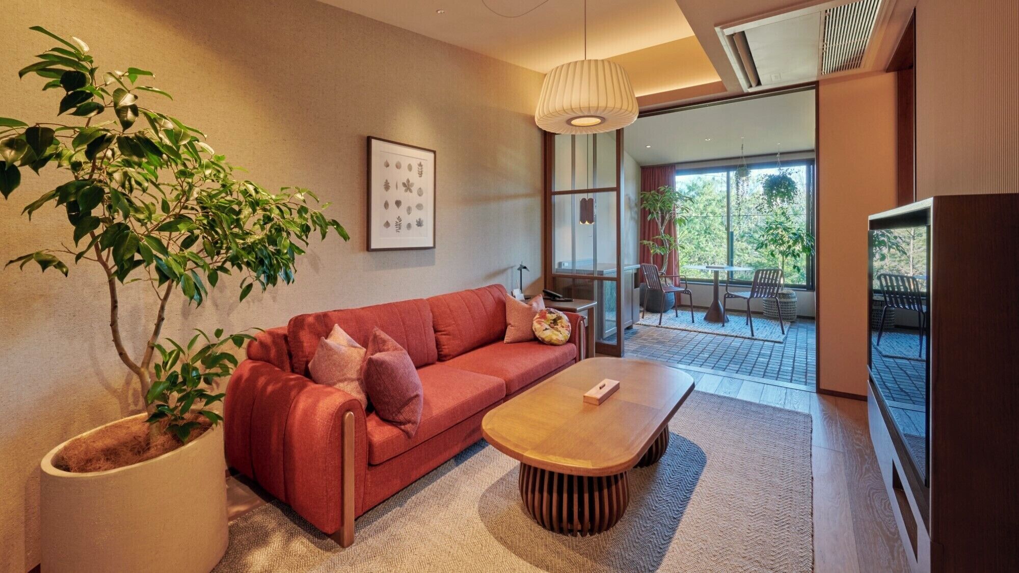 Un salon moderne avec un canapé rouge, une table basse en bois, une grande plante en pot et un tableau encadré au mur.