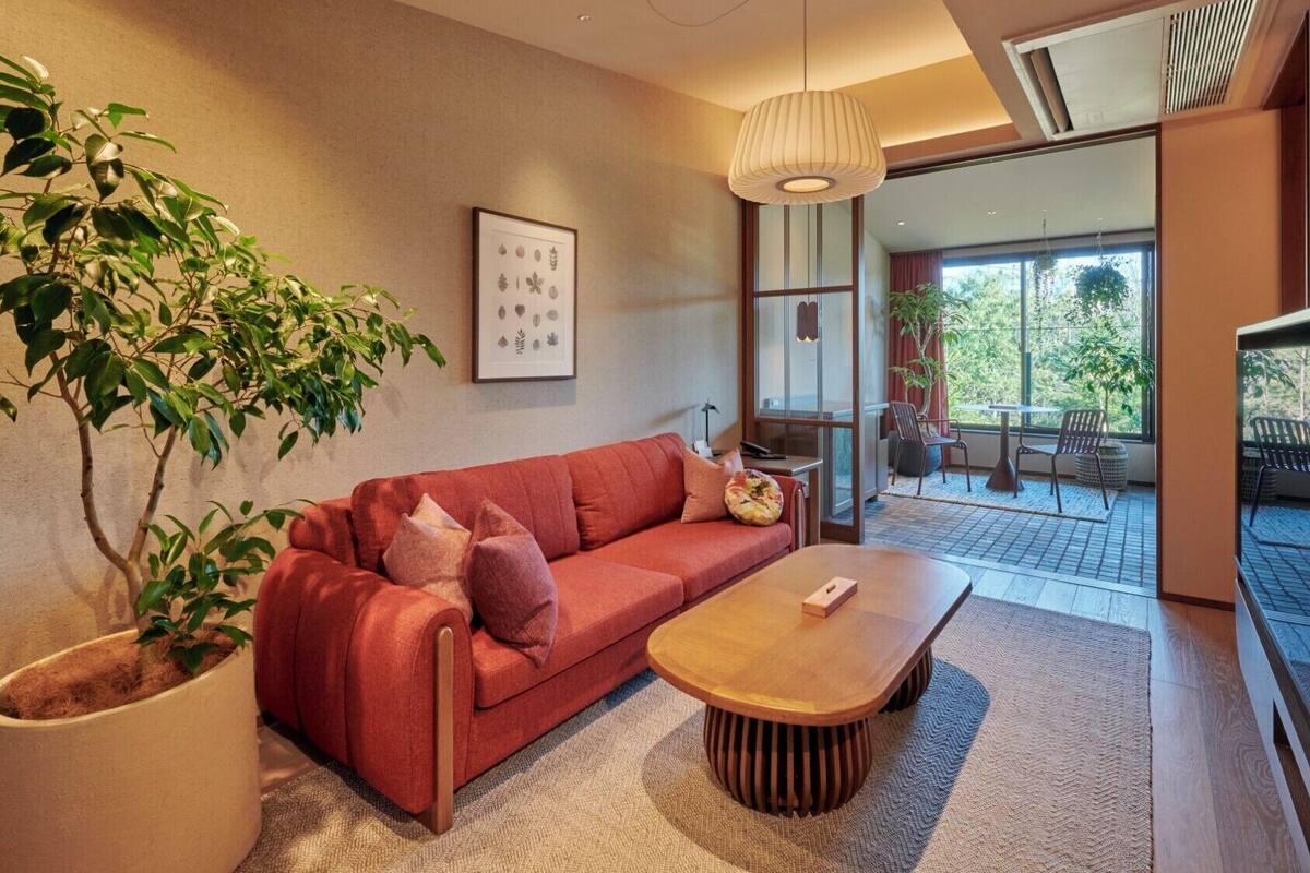 Uma sala de estar moderna com um sofá vermelho, uma mesa de centro de madeira, uma grande planta em vaso e um quadro na parede.