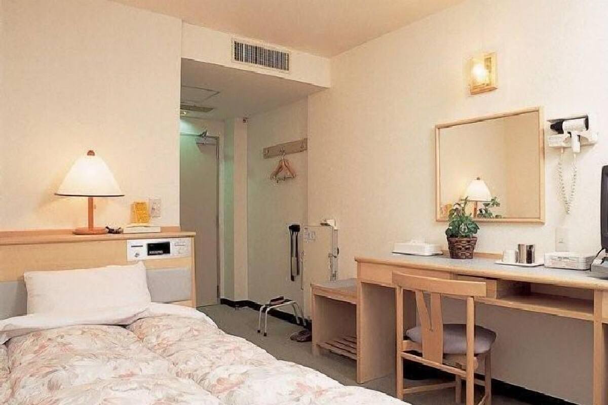 Una habitación de hotel con cama, escritorio, silla, lámpara y espejo.