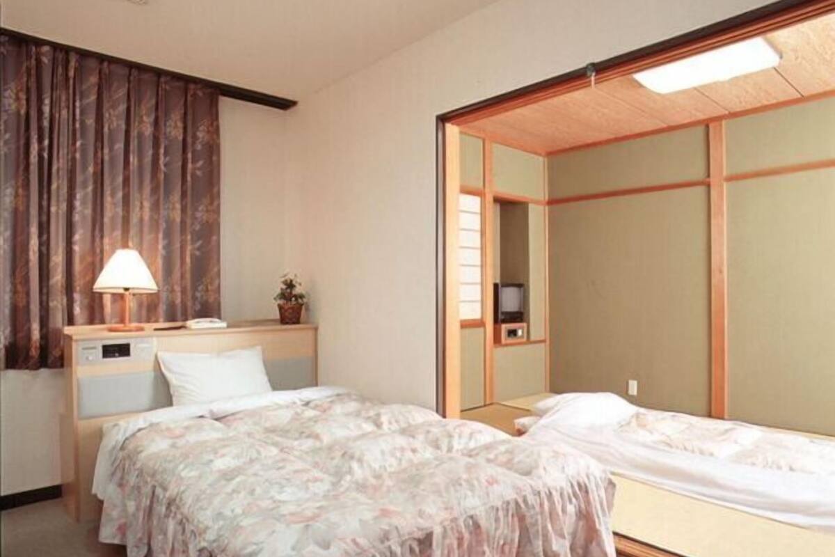 Una habitación de hotel con dos camas, una mesita de noche con lámpara, una planta pequeña y un televisor.
