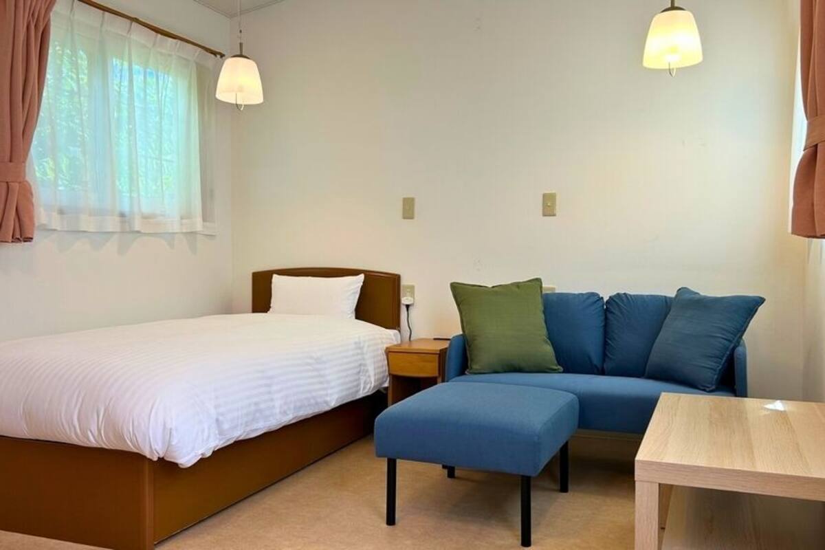 A bedroom with a bed, a sofa, a small table, and two pendant lights.