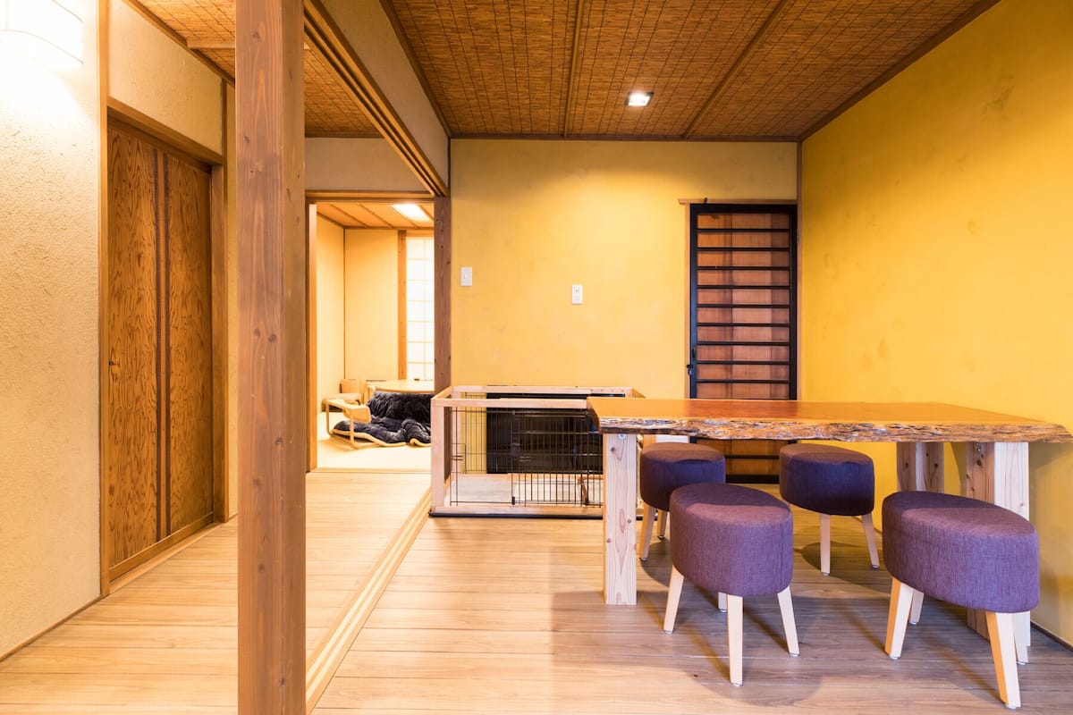 A room with a wooden floor, a table with four chairs, a bed, and a sliding door.