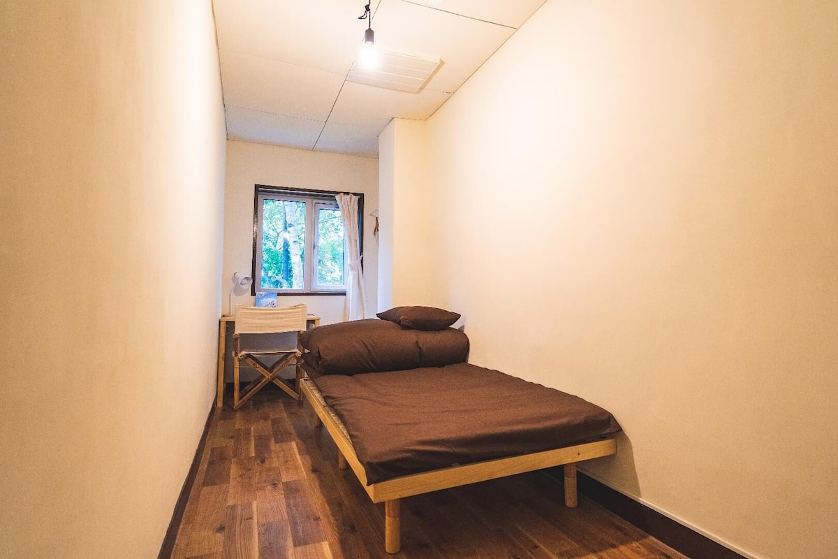 Una habitación pequeña con cama, un escritorio y una ventana.