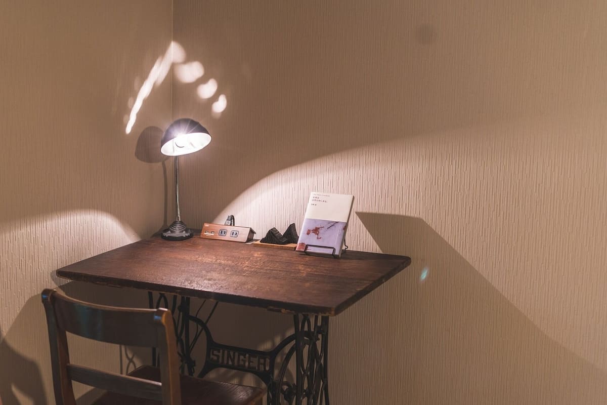 Una mesa de madera con una lámpara, un distribuidor de corriente y un libro encima.