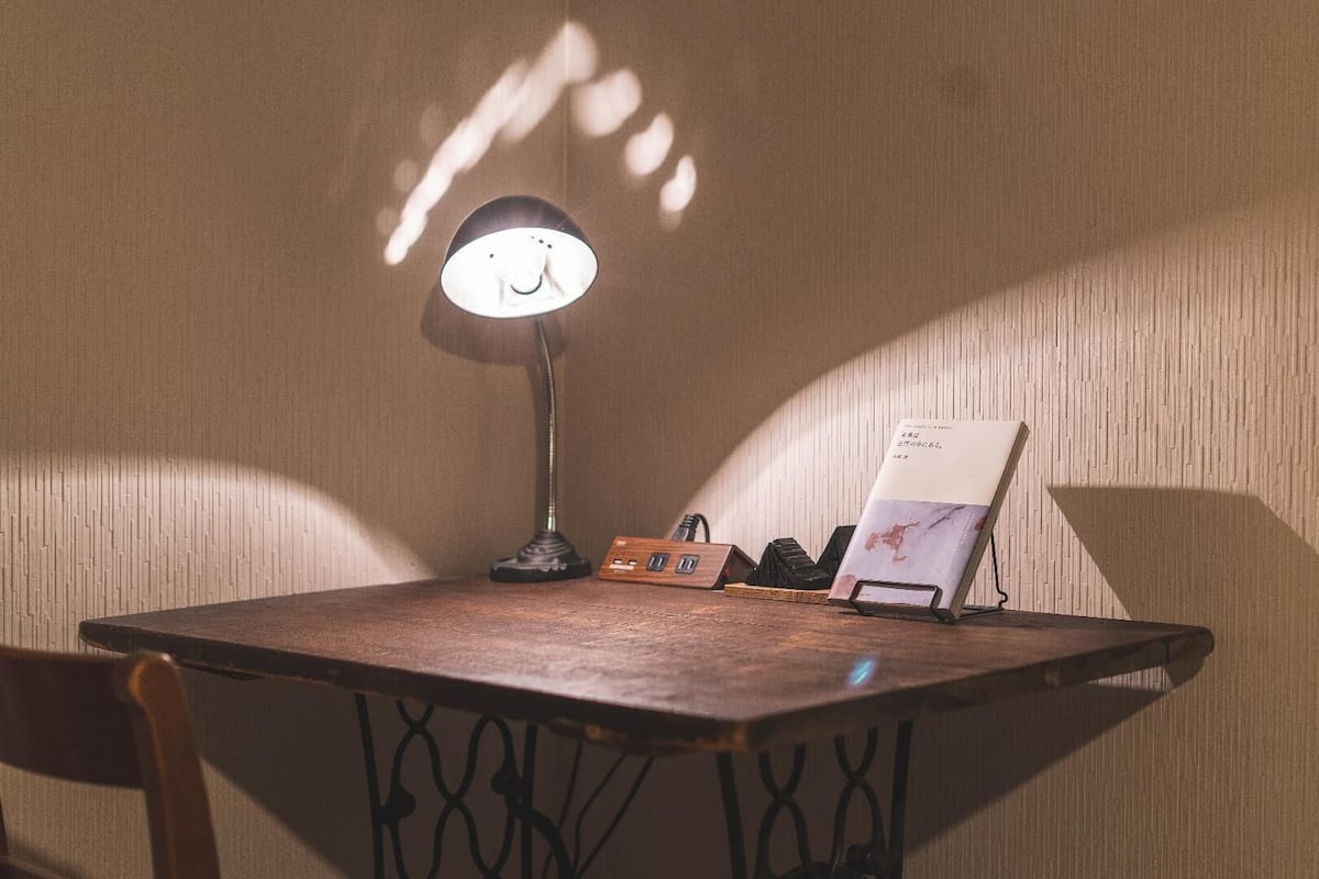 Una mesa de madera con una lámpara de escritorio, una pequeña caja de madera y un libro sobre un atril.