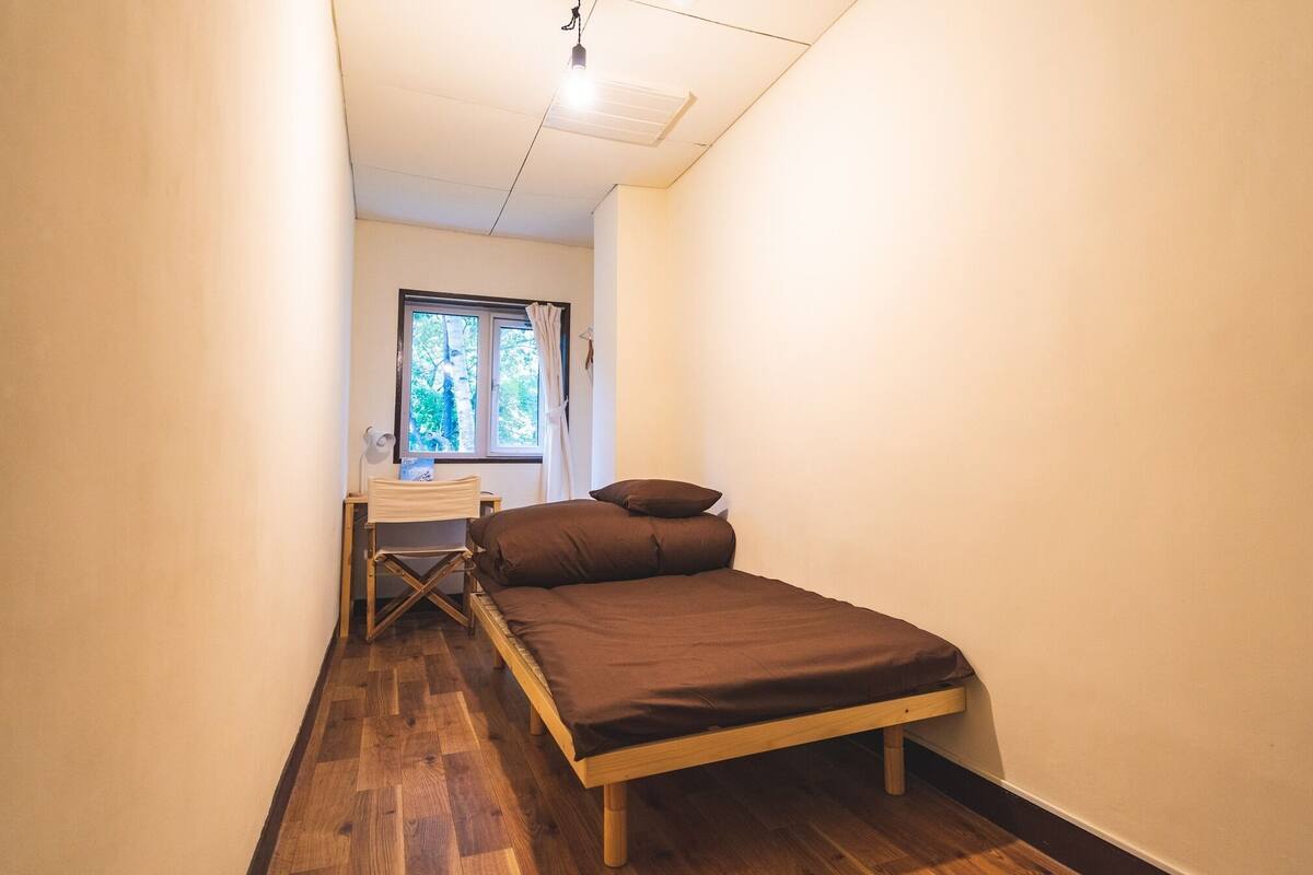 Una habitación pequeña y estrecha con una cama, un escritorio y una ventana.
