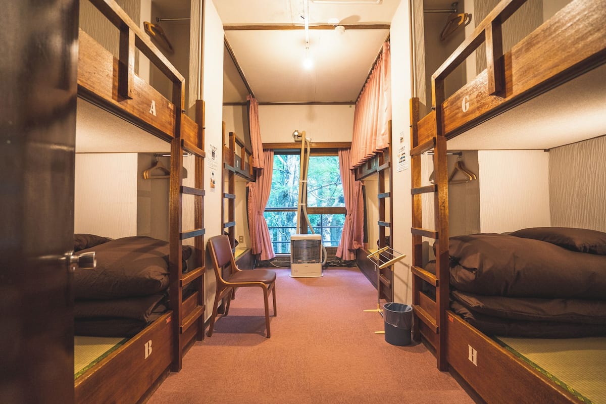 Un dormitorio con literas, una silla, un equipo de aire acondicionado y una ventana con cortinas.