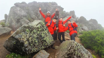 A group of people in red jackets posing on a rocky terrain with large boulders and greenery.