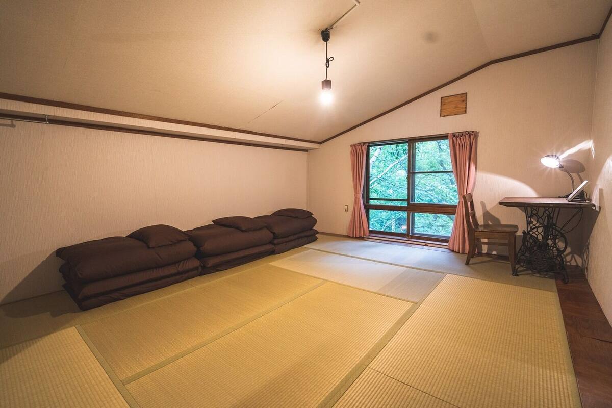 Una habitación con esteras de tatami, un sofá, un escritorio con lámpara y una ventana con cortinas.