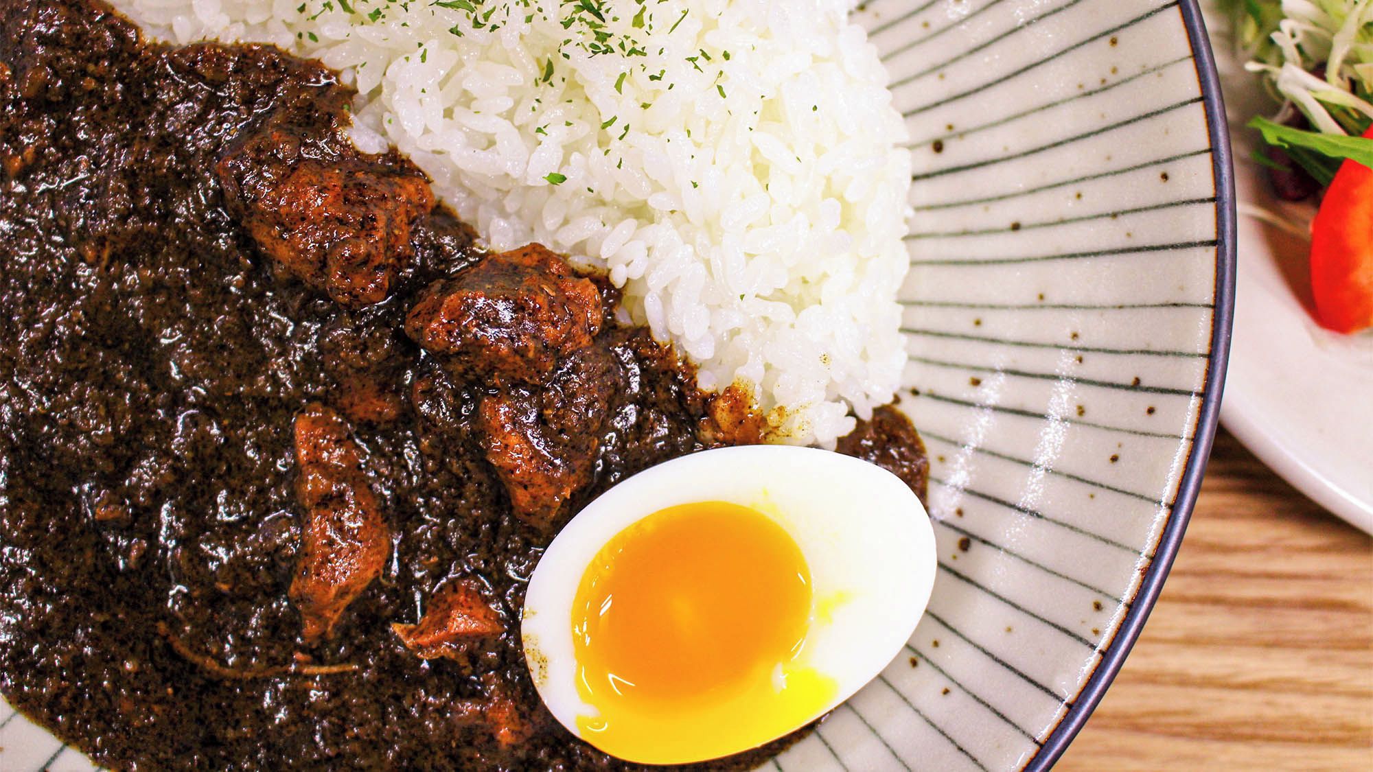 A plate with a meat dish, rice, and a half-boiled egg.