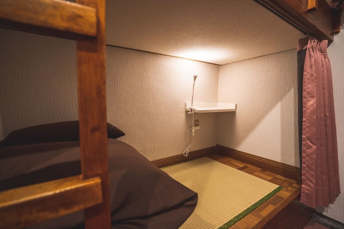 Una habitación pequeña y acogedora con una cama litera, una mesita de noche, un estante en la pared y un enchufe.