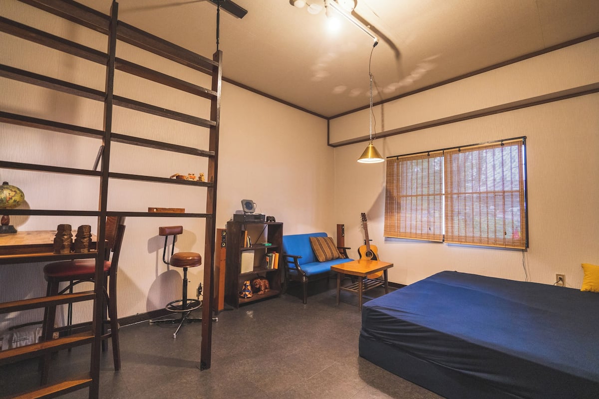 Una habitación con una cama, un escritorio, una silla, una estantería y una ventana con persianas.