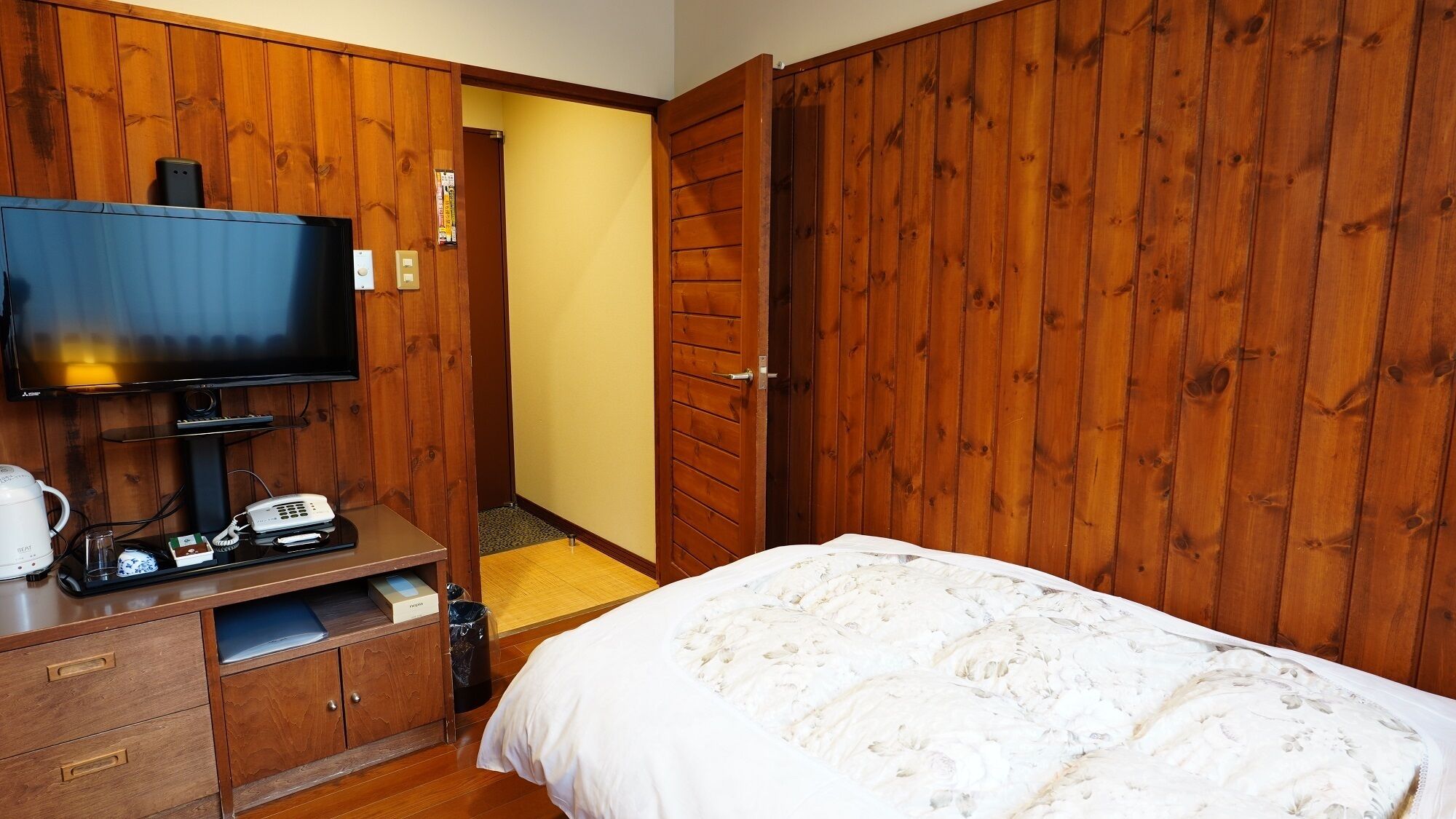 A hotel room with a bed, a television, a coffee maker, and a desk with a telephone.