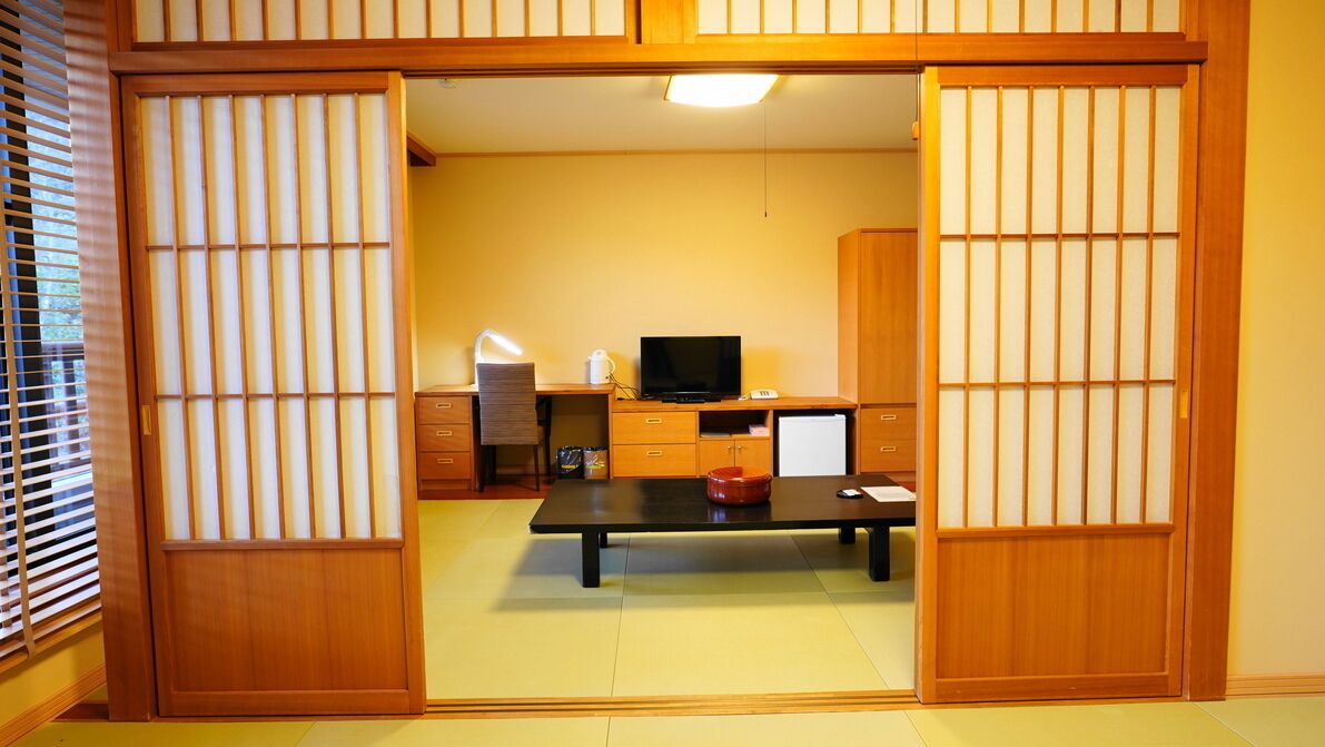 Um quarto japonês tradicional com tatames, uma mesa baixa, uma televisão e portas deslizantes.
