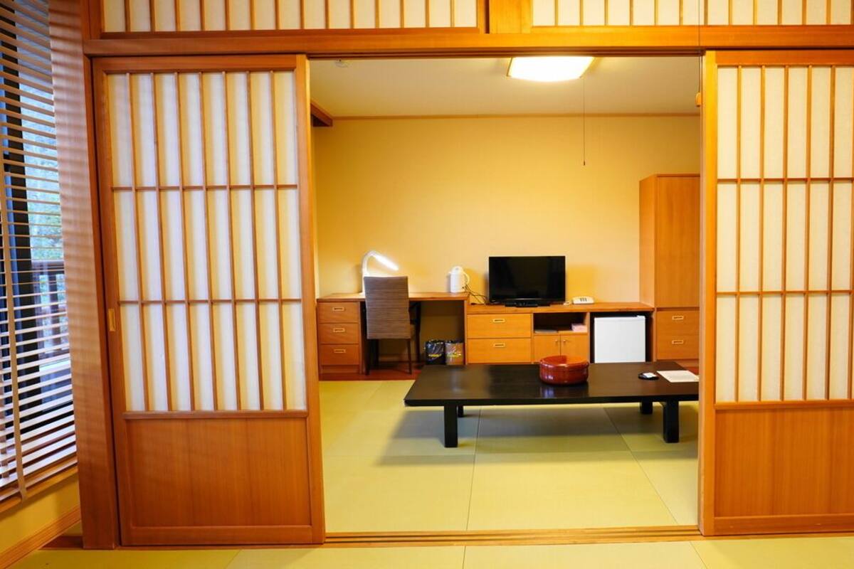 A traditional Japanese room with tatami flooring, a low table, a television, and sliding doors.
