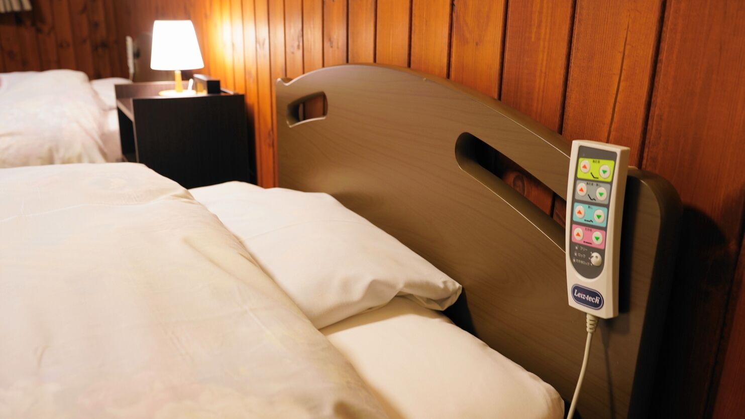 Uma cama com painel de controle fixado na cabeceira, uma mesa de cabeceira com abajur e painéis de madeira na parede.