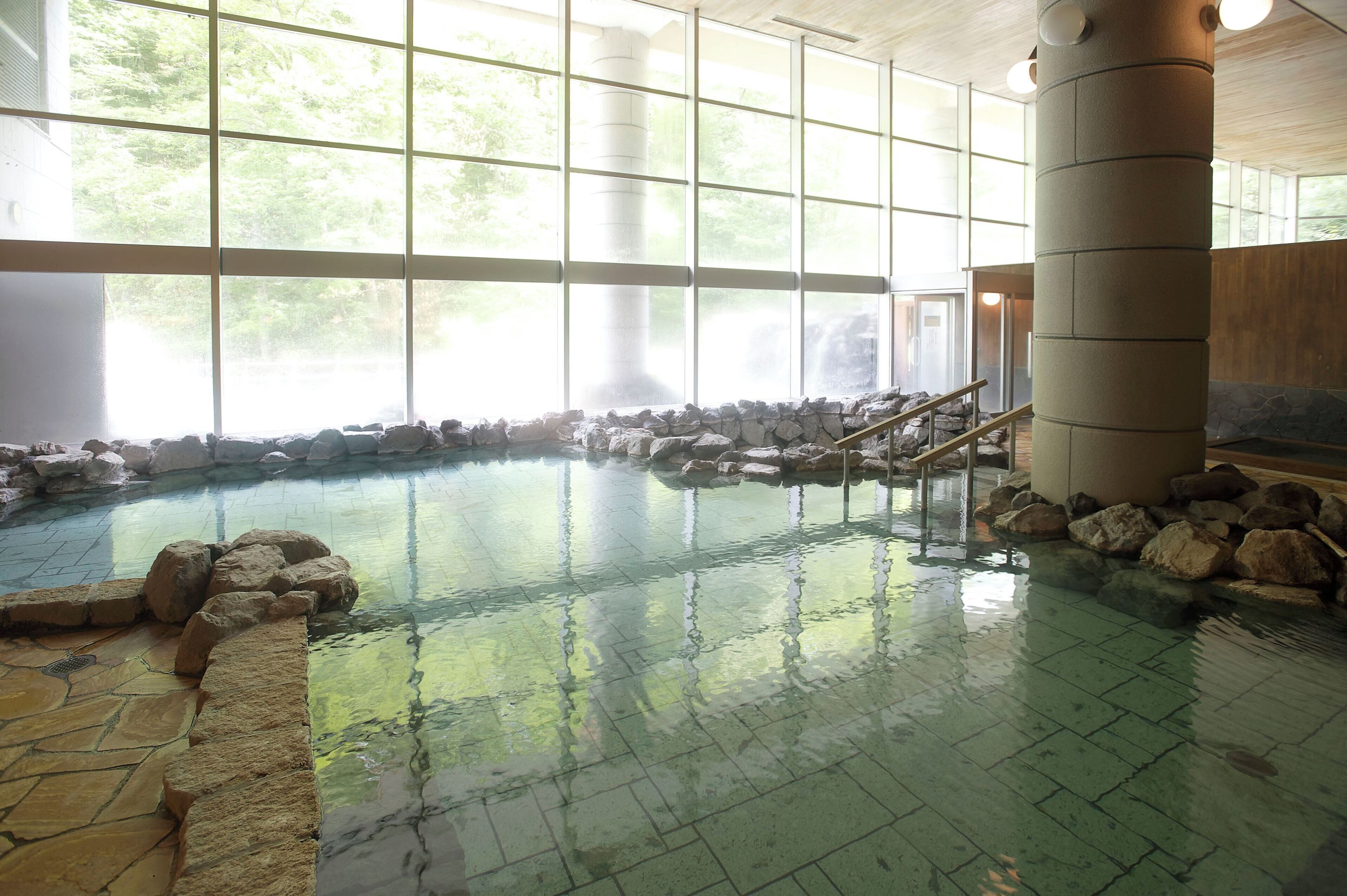 An indoor swimming pool with stone walls, a wooden staircase, and large windows.