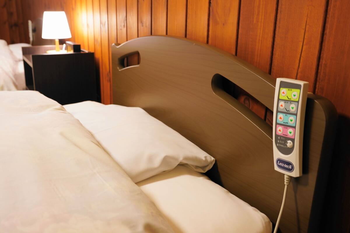 A hotel room with a bed, a bedside table with a lamp, and a control panel on the headboard.