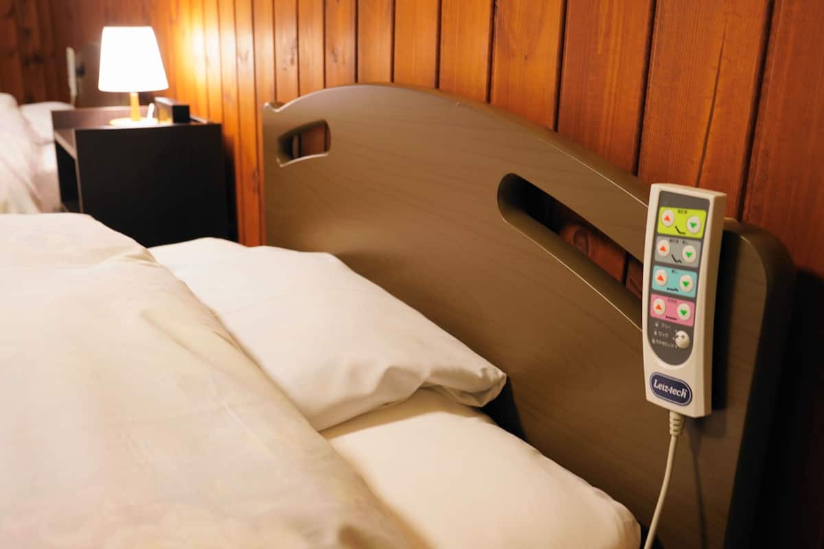 A hotel room with a bed, a bedside table with a lamp, and a control panel on the headboard.