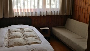 Um quarto com cama, sofá, uma mesinha e janela com cortinas.