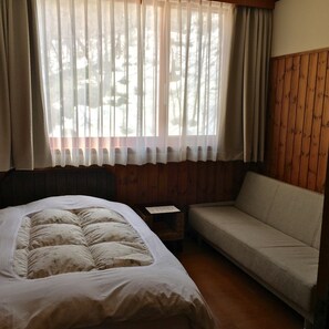 Um quarto com cama, sofá, uma mesinha e janela com cortinas.