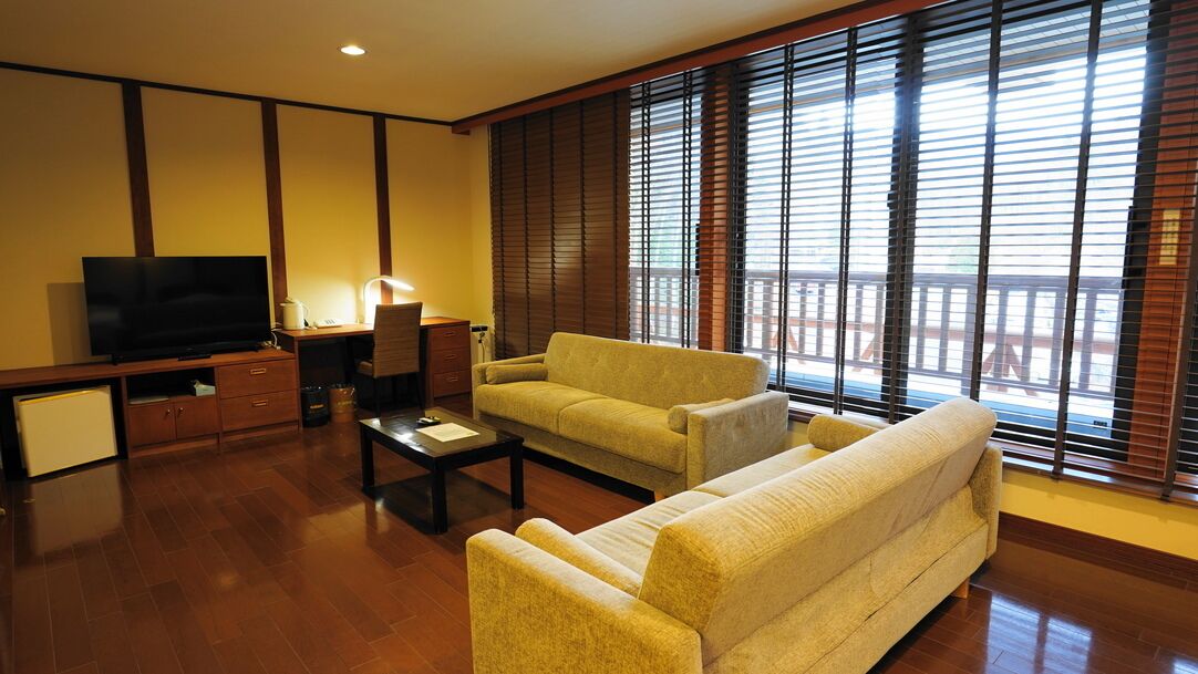 A living room with a sofa, a coffee table, a TV, and a desk with a lamp.