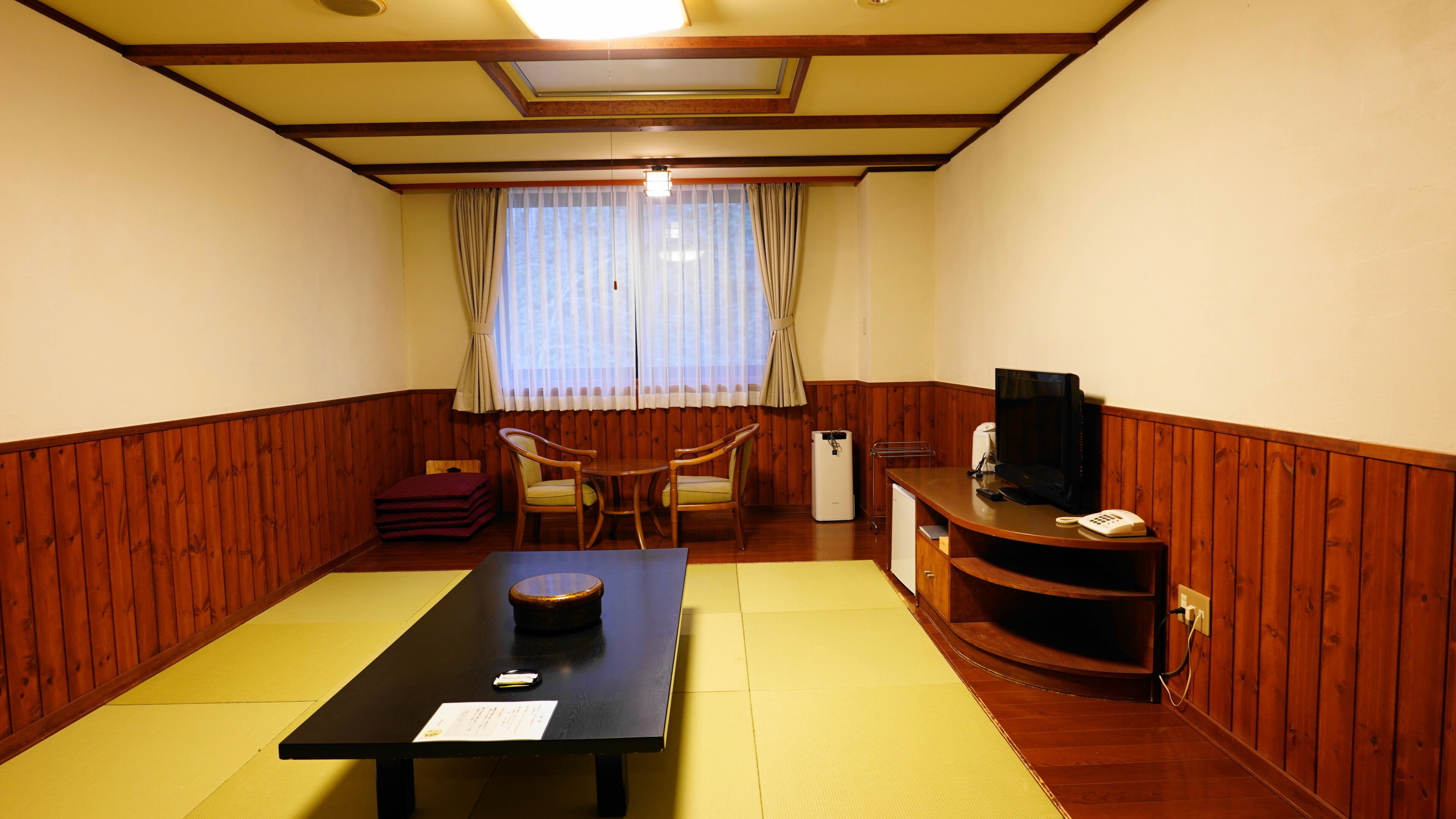 A room with a tatami mat floor, a low table with a placemat, a chair, a small cabinet, and a television on a wooden stand.