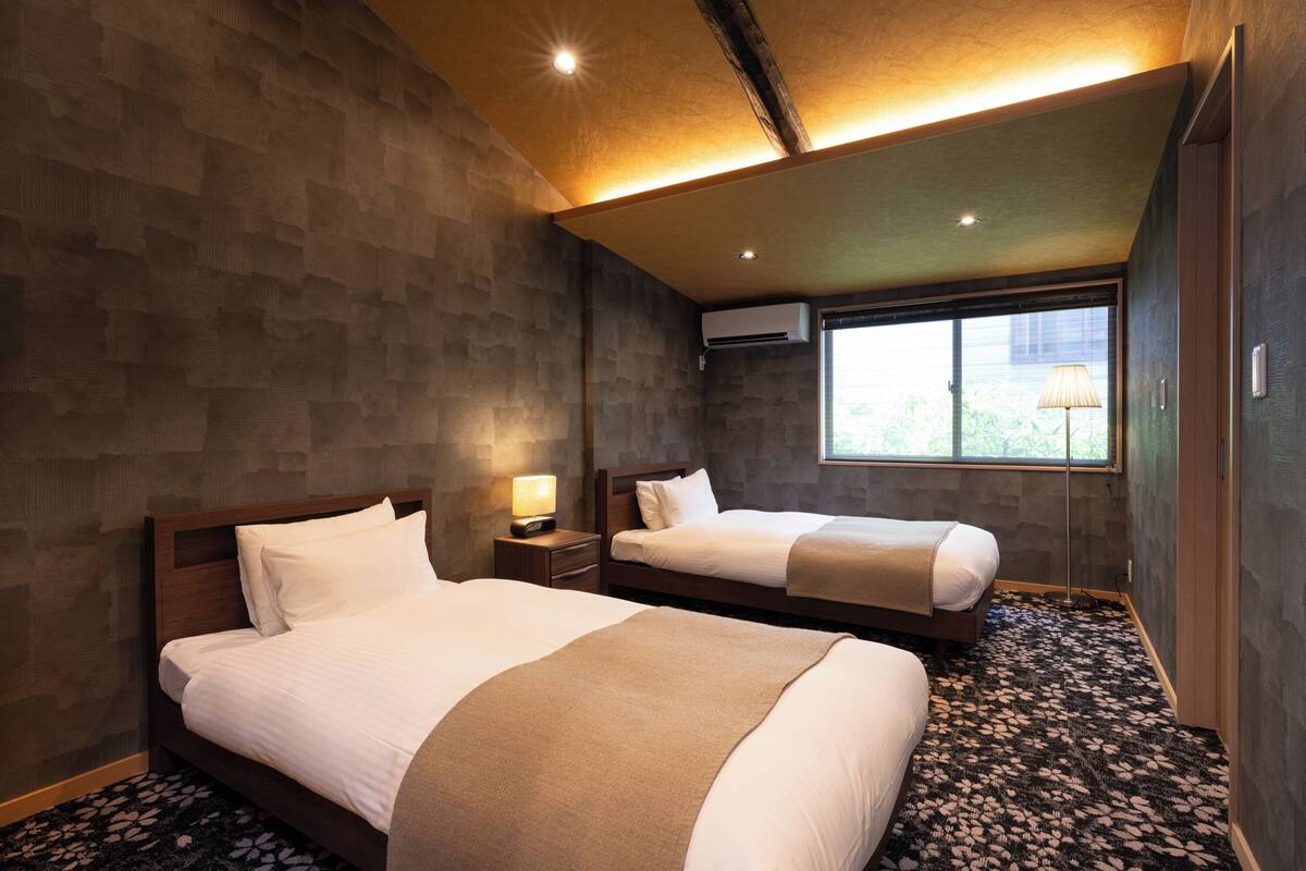 Habitación de hotel con dos camas, una ventana, aire acondicionado y una lámpara.