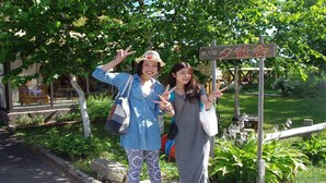 Two individuals posing in front of a sign with Japanese characters, indicating a location.