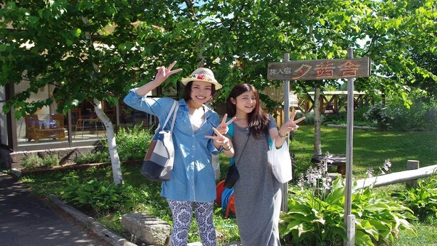 Two individuals posing in front of a sign with Japanese characters, indicating a location.