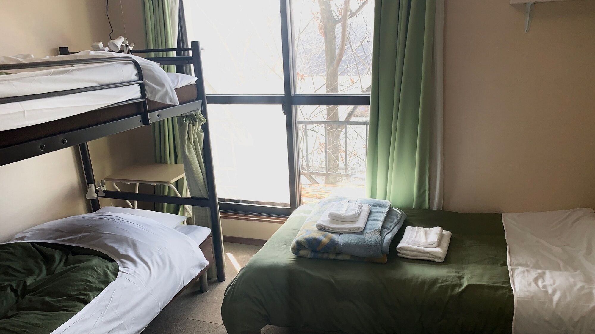 Een slaapkamer met stapelbed, een raam, een stoel en een bed met een groene deken.
