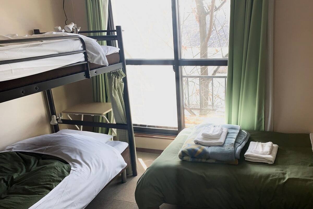 Camera con letto a castello, una finestra, una sedia e un letto con coperta verde.