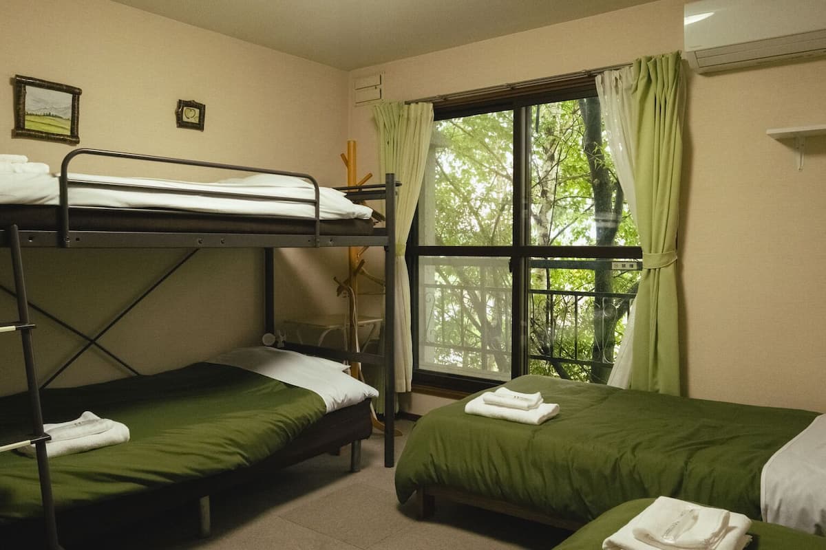 Una camera del dormitorio con letti a castello, una finestra con tende e un letto con copriletto verde.