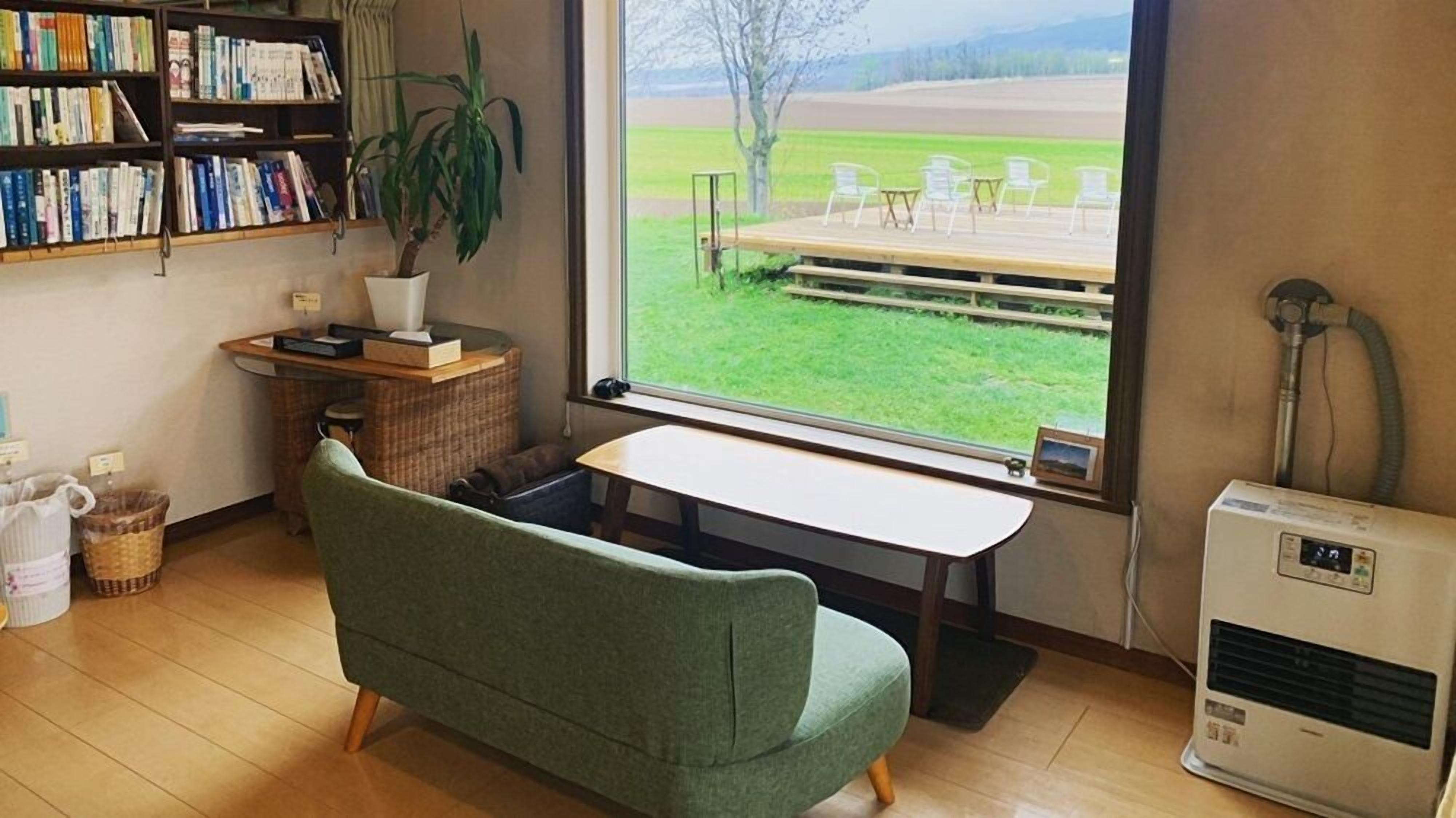 Een kamer met een groene bank, een houten bureau, een boekenplank, een plant in pot en uitzicht op een terras.
