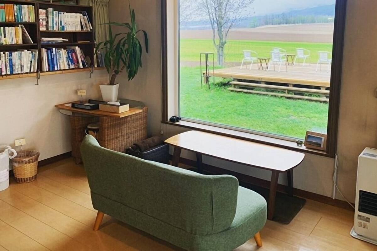 Una stanza con un divano verde, una scrivania in legno, una libreria, una pianta in vaso e vista su una terrazza esterna.