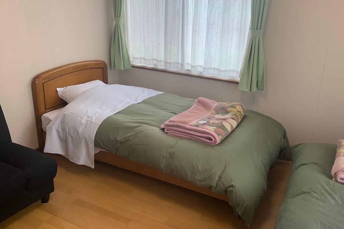 Un letto singolo con una testiera in legno, una coperta verde e una trapunta rosa.
